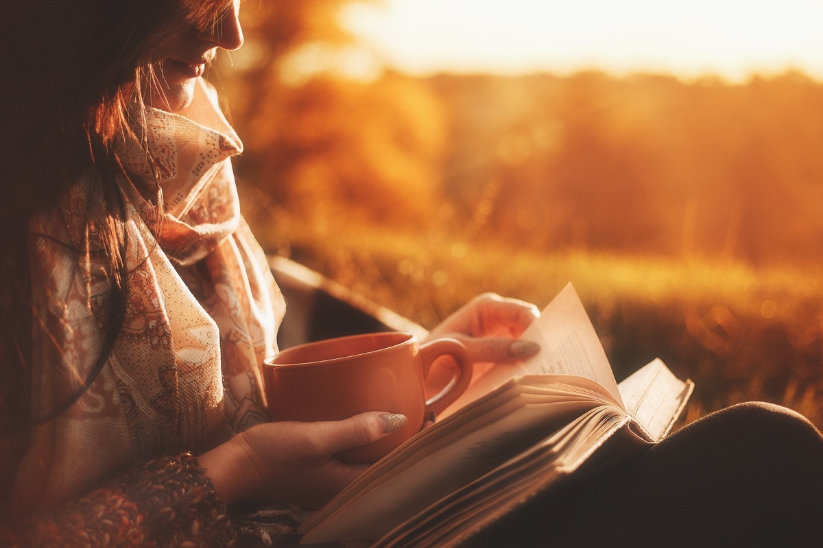 woman reading a book outside at sunset holding a cup of coffee - classic books