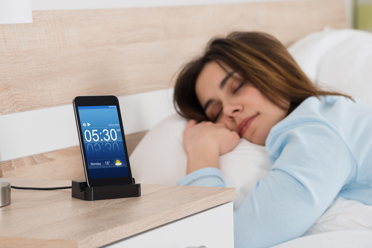 A young woman sleeping next to a smartphone charging on the nightstand