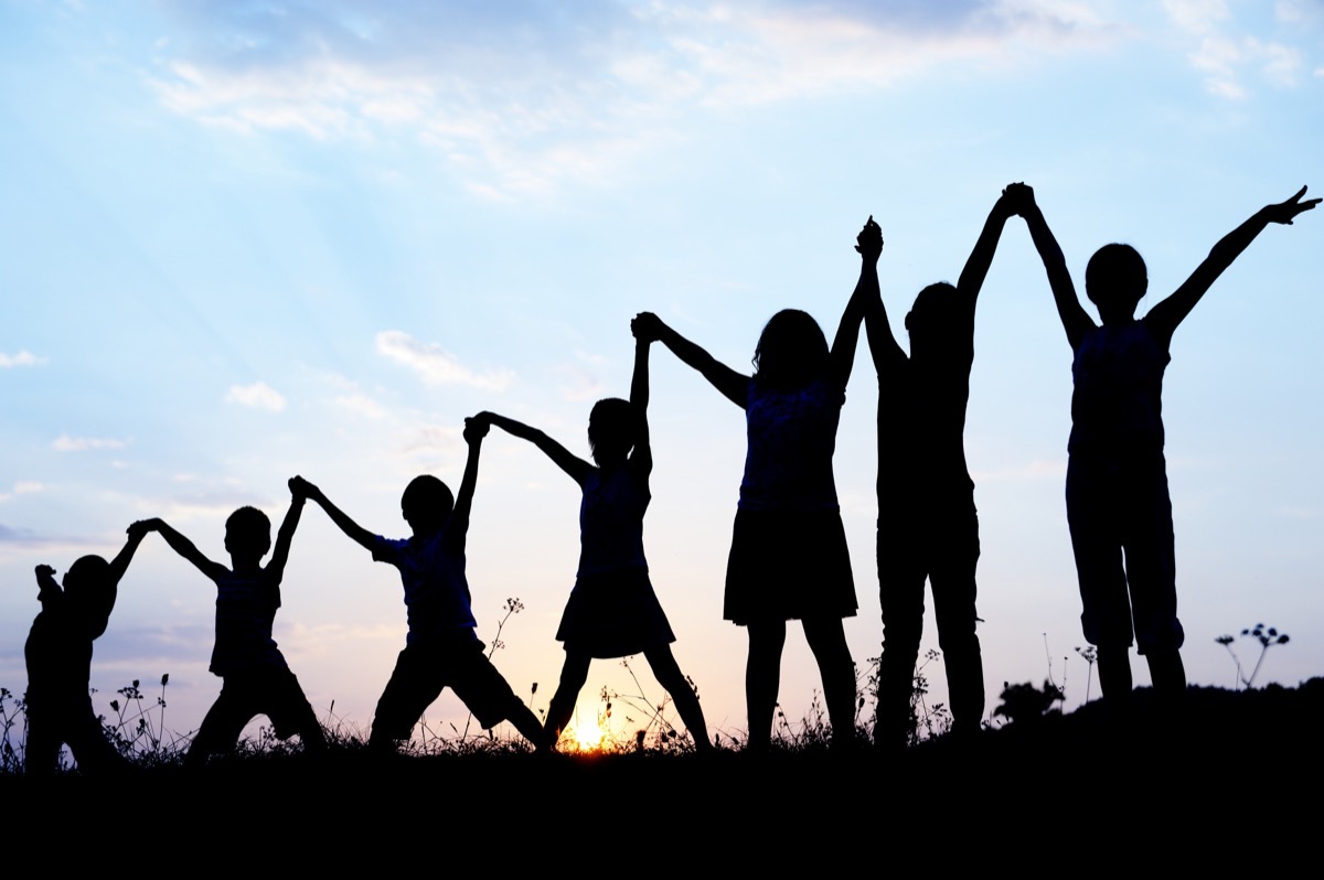 7 kids holding hands in a field at sunset silhouette