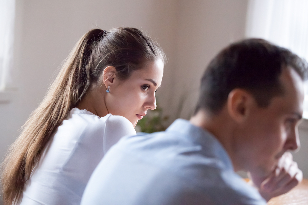 Back view of an offended woman looking at stubborn lover refusing reconcile after a fight