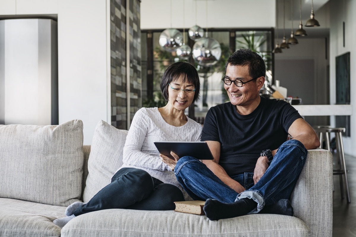 older asian man and woman on couch looking at a tablet together