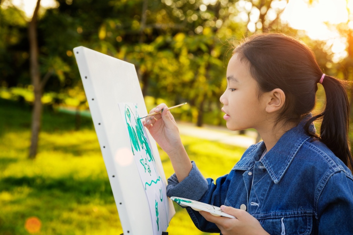 Young girl painting outside on a canvas