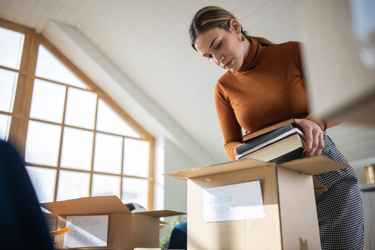 Selfless Caucasian female volunteer, packing books and toys for donation into cardboard box