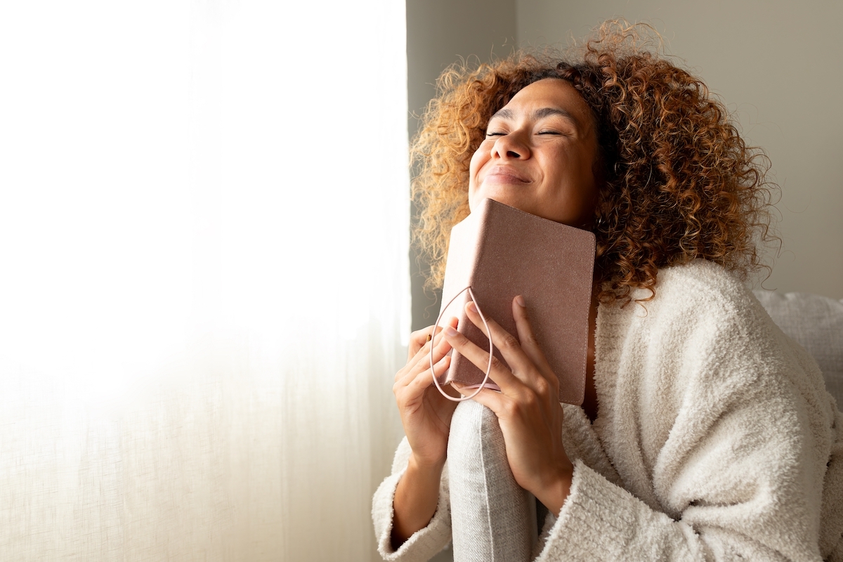 Happy woman dressed in beige smiling with her eyes closed while holding a journal