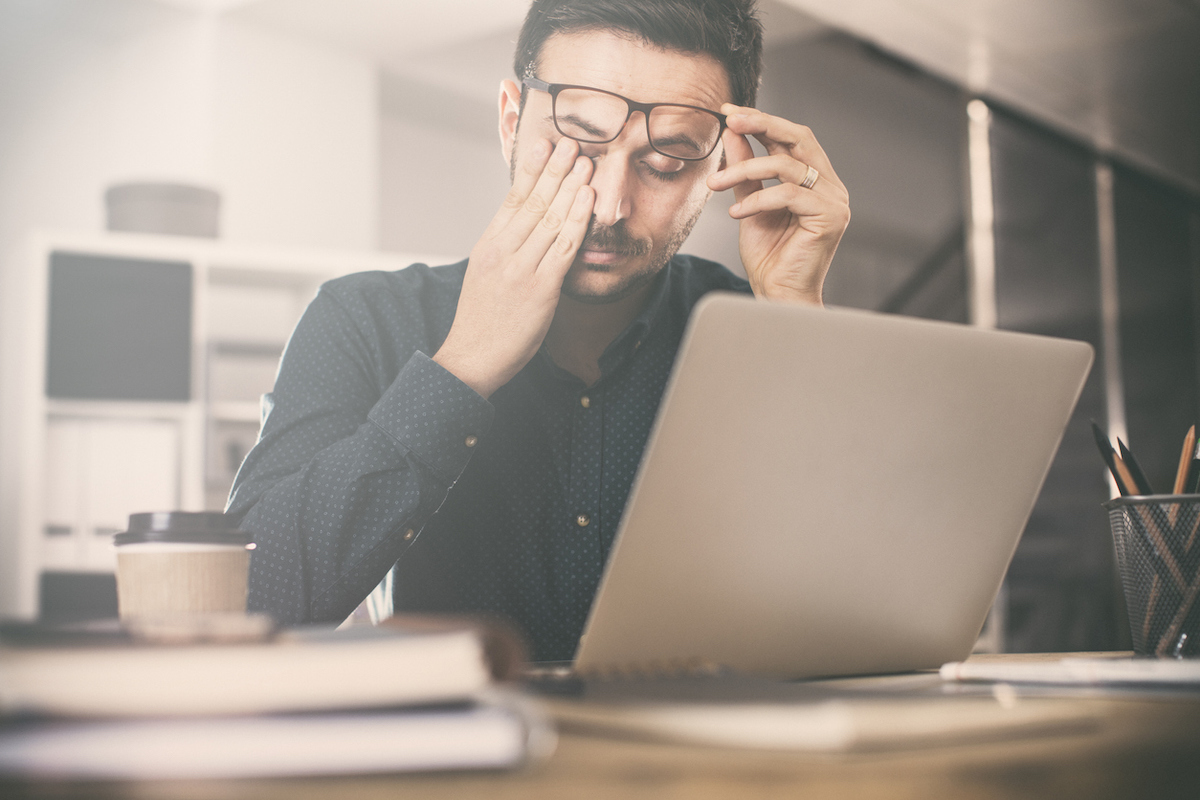 Tired young man rubbing his eyes in front of a computer