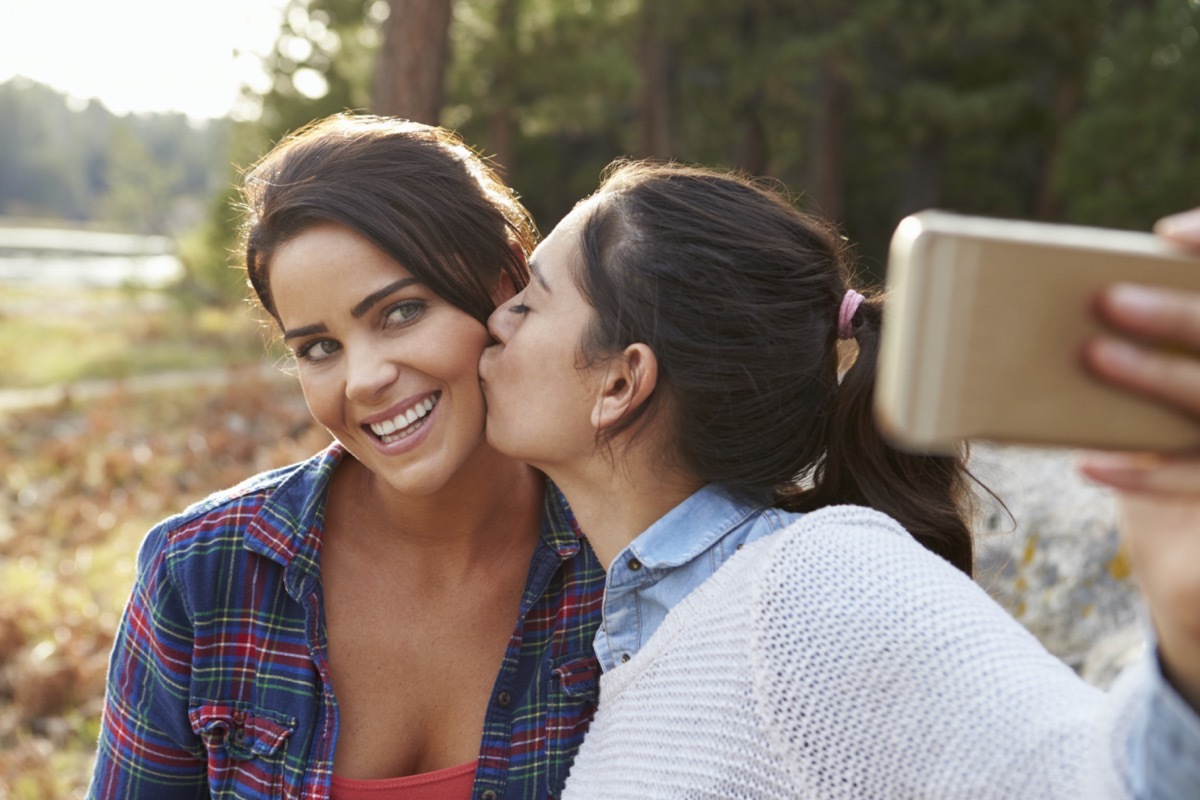 Woman kissing girlfriend on cheek and taking selfie