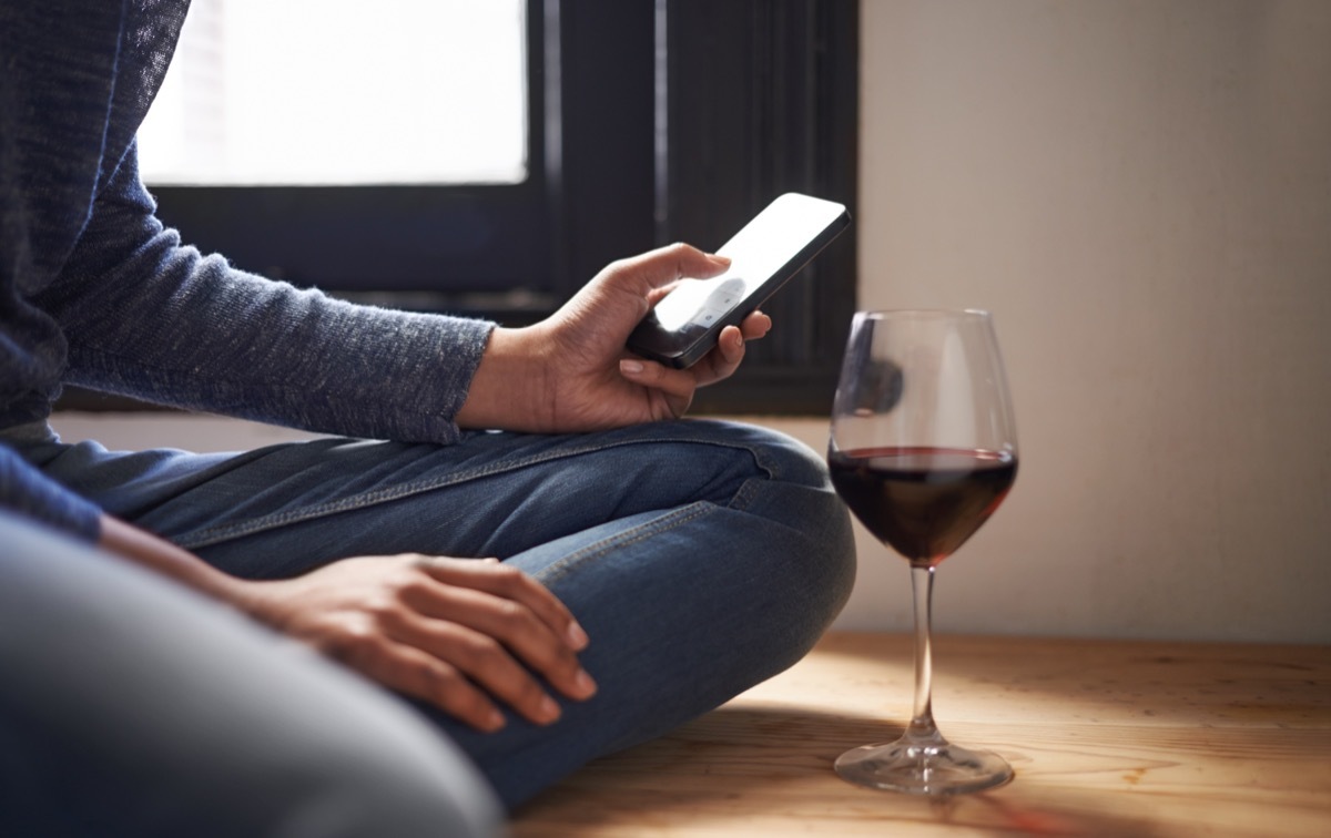 Cropped shot of a woman sending a text message with a glass of wine beside her