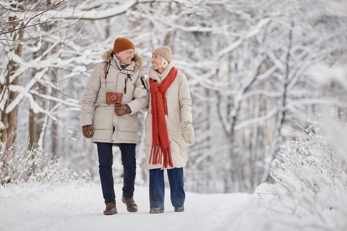 Full length portrait of happy senior couple enjoying walk in winter forest and looking at each other with love