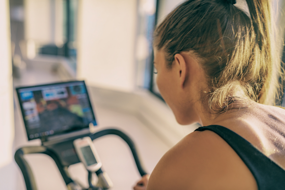 woman training on stationary bike equipment indoors while watching class on screen