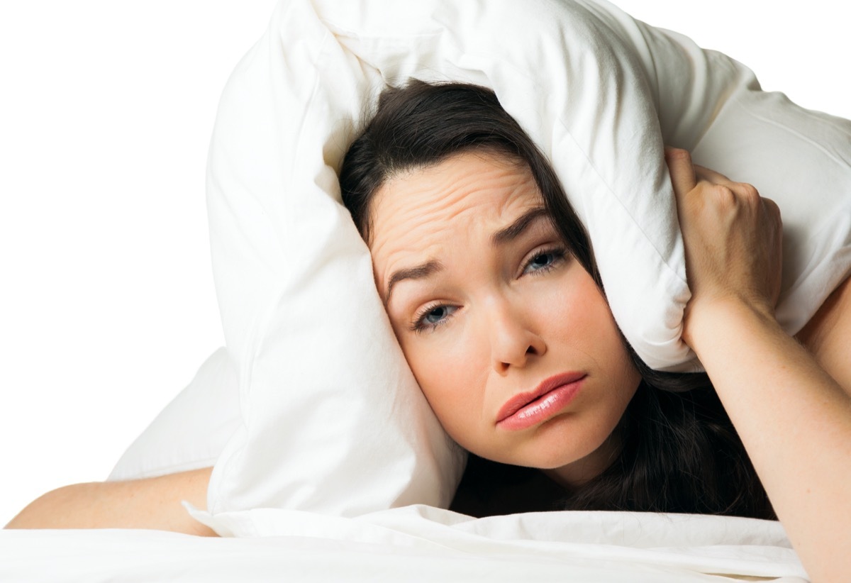 A tired sleepless woman with the pillow over her head