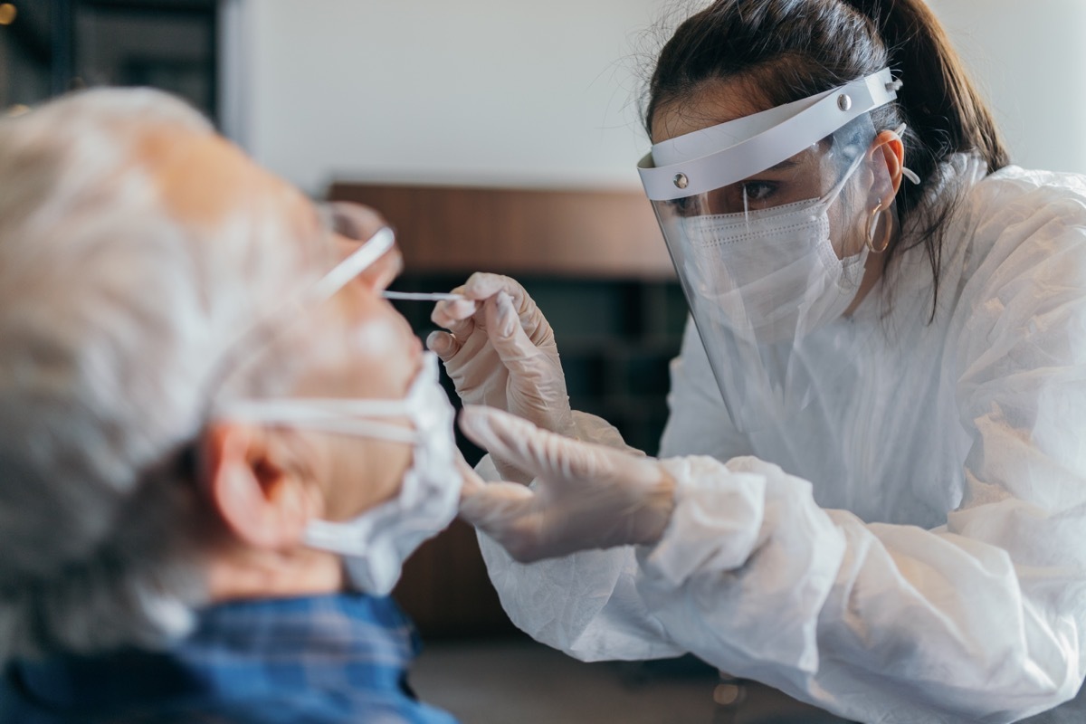 Female doctor in protective suit taking nose swab test from senior man