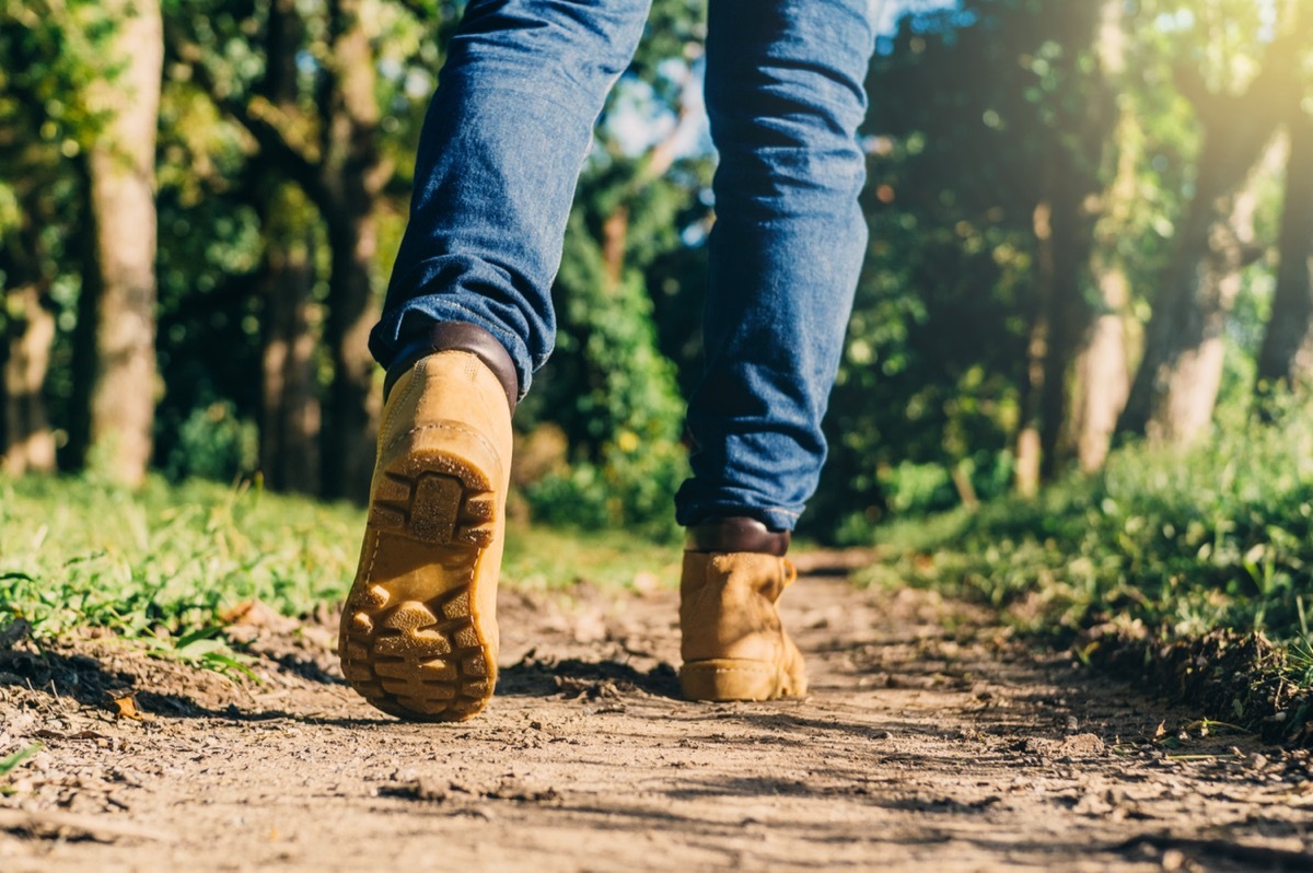 feet of an adult wearing boots to travel walking in a green forest. travel and hiking concept.