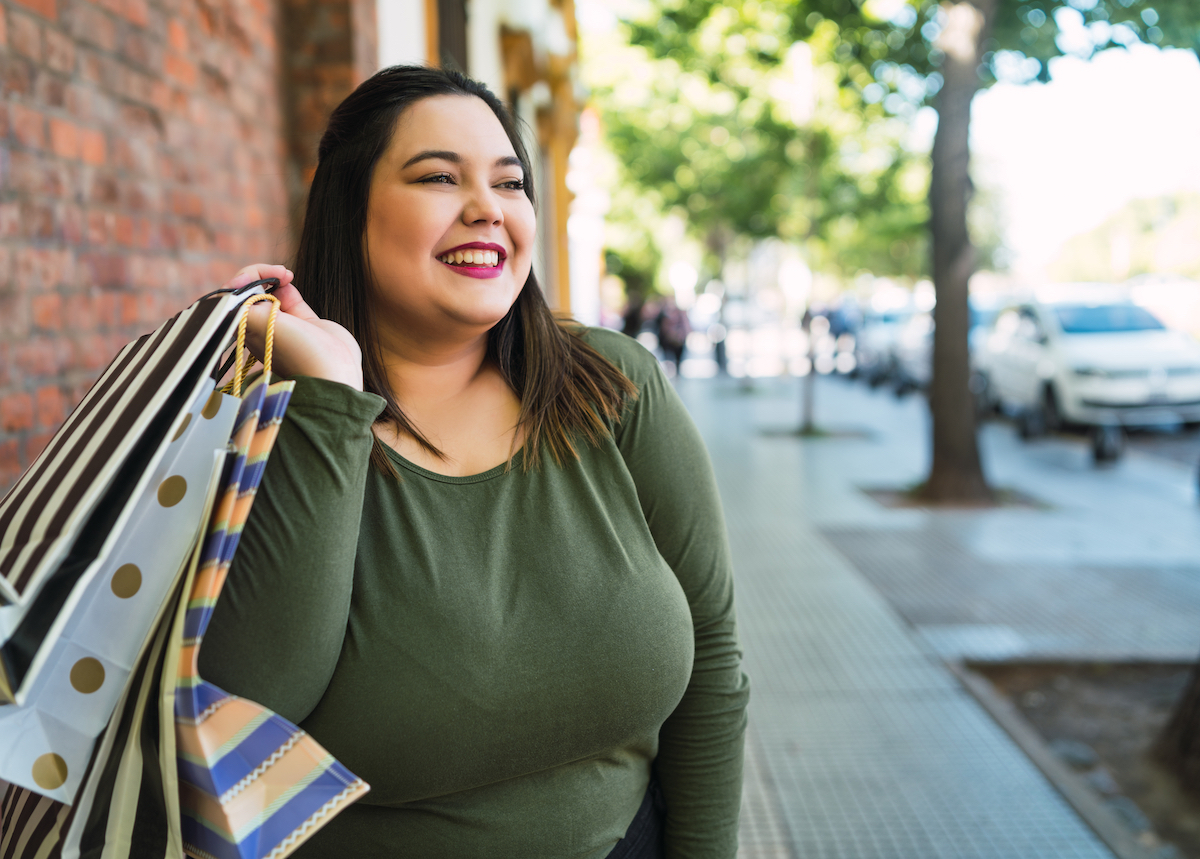 Portrait of young plus size woman holding shopping bags outdoors on the street.