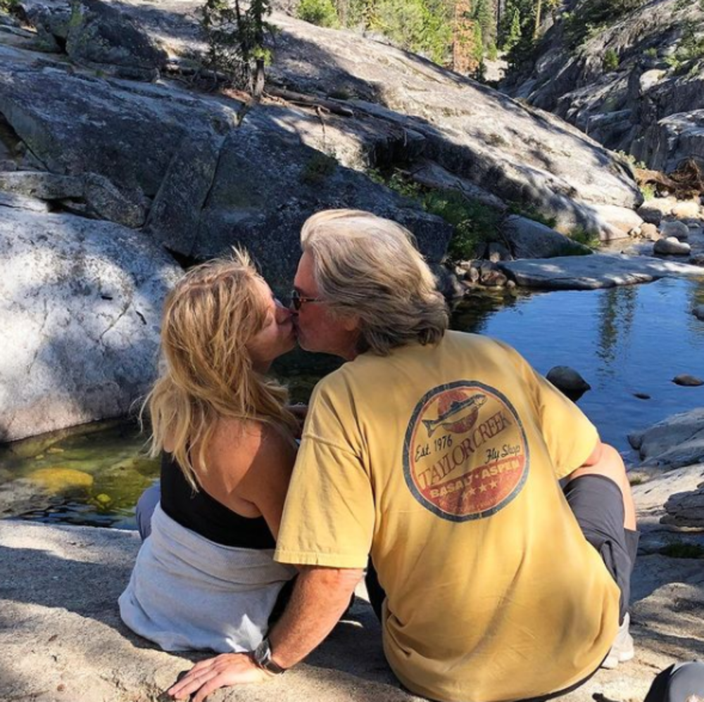 Goldie Hawn and Kurt Russell kissing while sitting near a stream