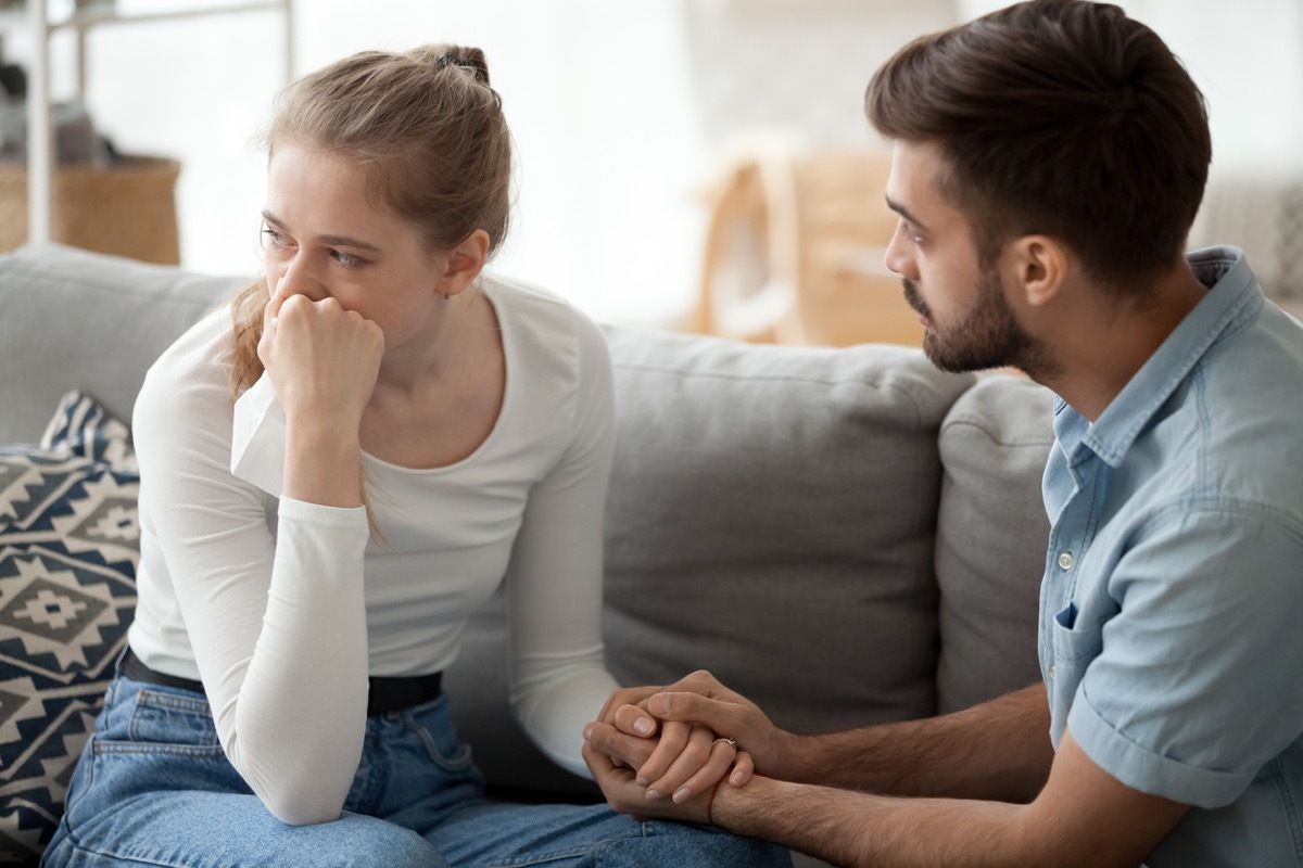 Loving young husband hold crying wife hand showing empathy and support, millennial couple sit on couch at home reconcile after fight, caring man making peace with beloved woman. Relationships concept