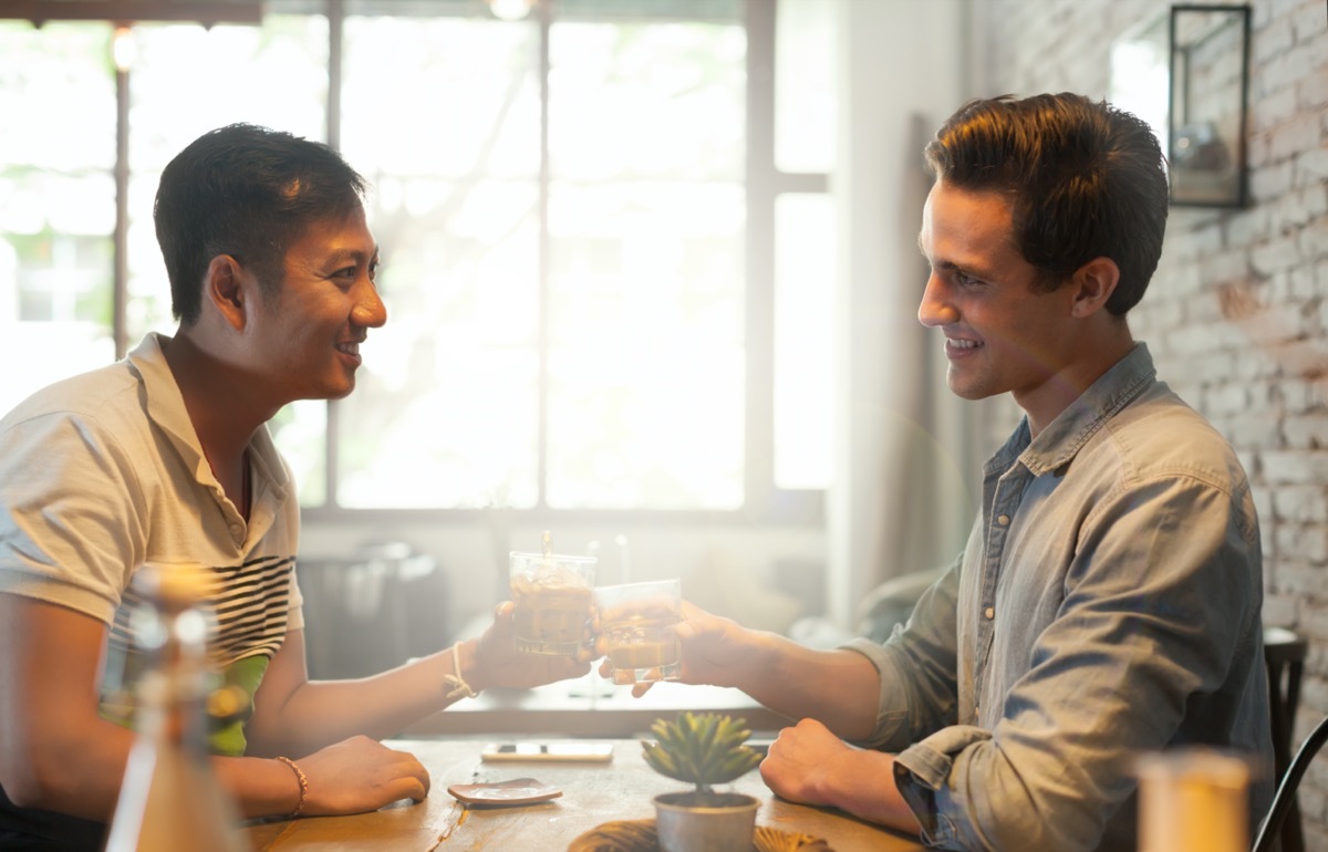 Two young men clinking glasses across a table