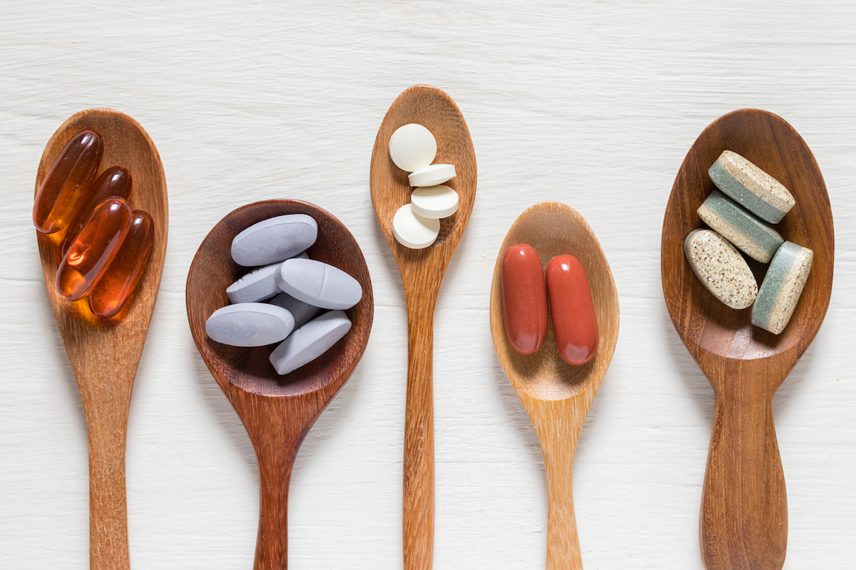 Variety of vitamin pills in wooden spoon on white background