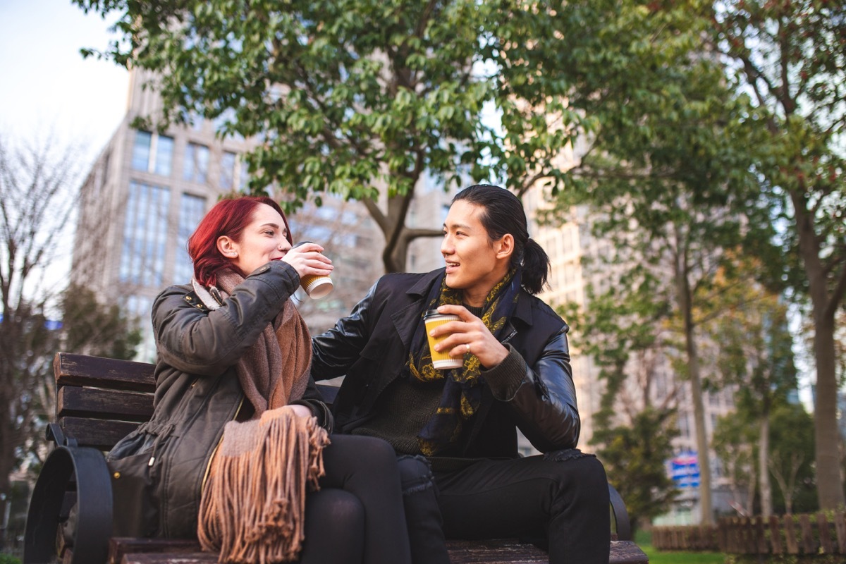 two friends sitting on a park bench drinking coffee