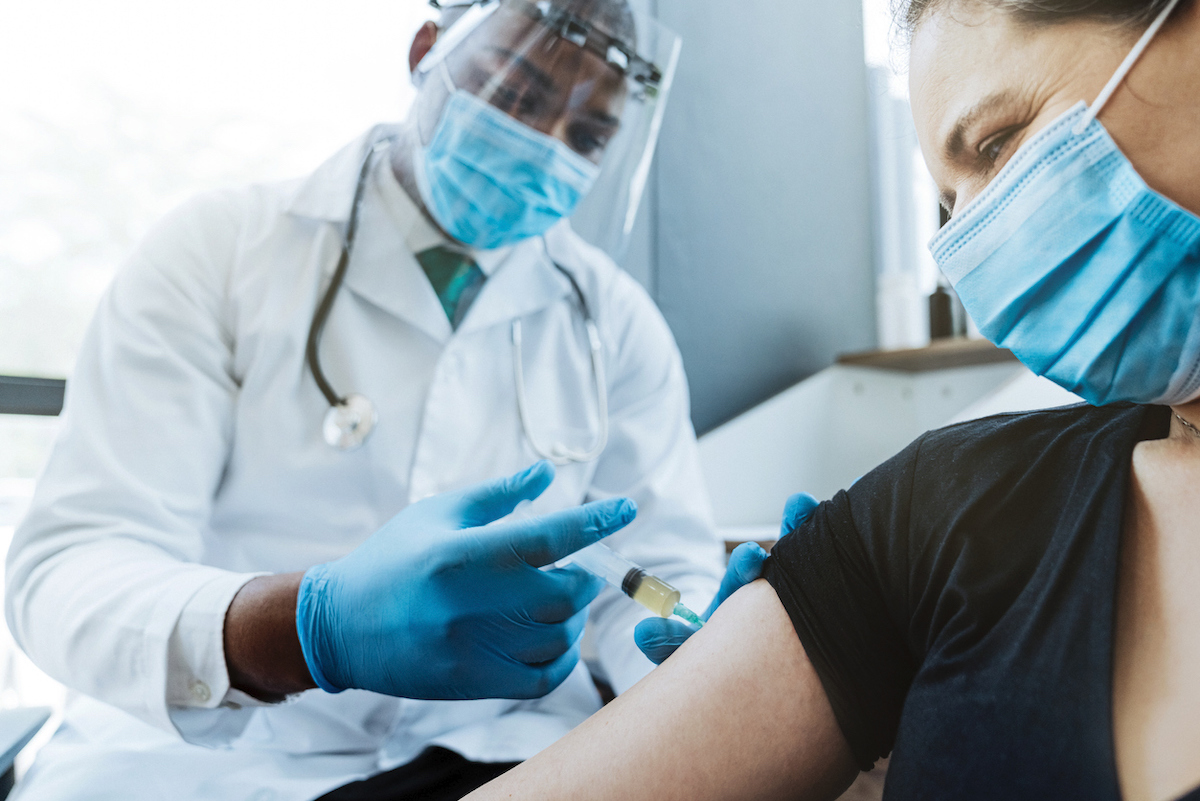 Healthcare worker injecting COVID vaccine in female patient's arm at medical clinic.