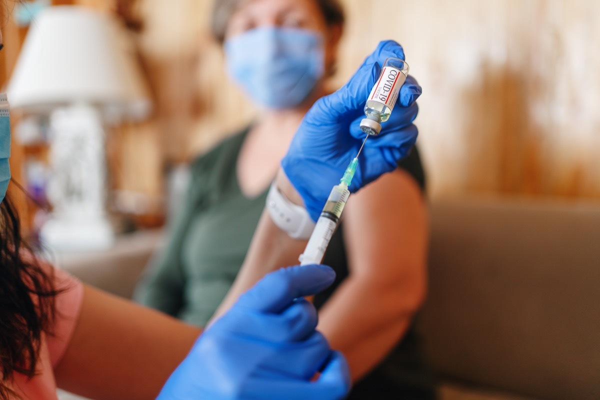 General practitioner vaccinating old patient at home with copy space. Doctor giving injection to senior woman at home. Nurse holding syringe and using cotton before make Covid-19 or coronavirus vaccine.