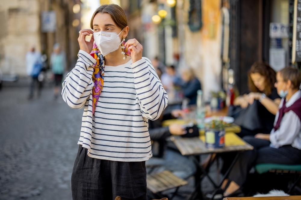 A young woman putting on a face mask on the street