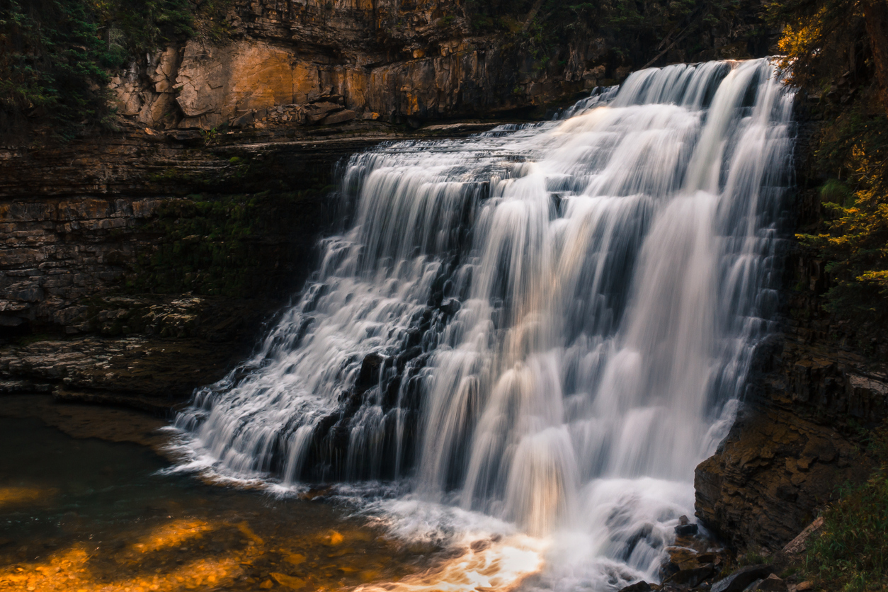 Fresh mountain water flows over the cascade of Ousel Falls in Montana as golden sunlight highlights the scene. Natural beauty background with copy space.