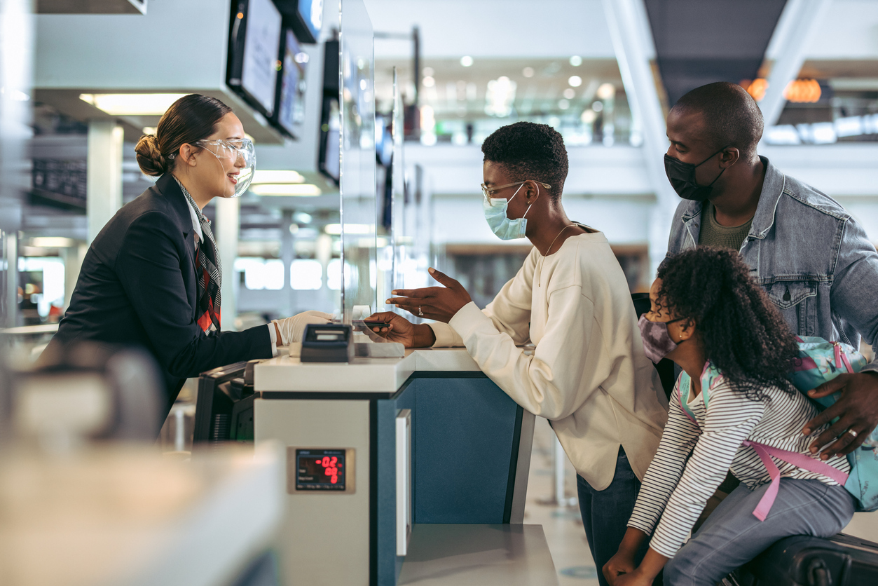 A family wearing face masks speaks with a ticket agent at the airport