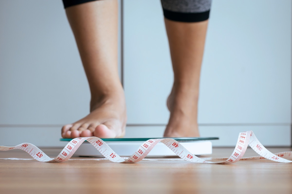 Woman stepping on scale with measurement tape