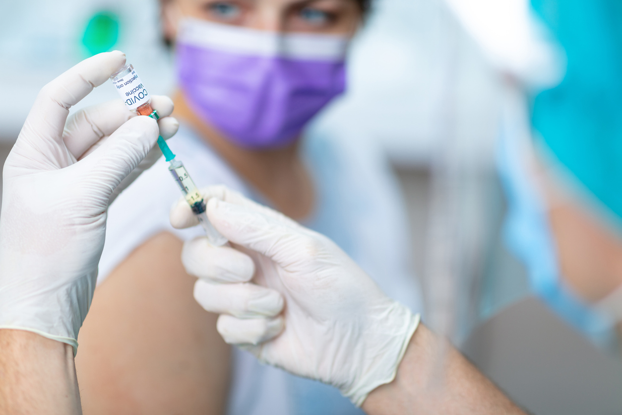 A doctor wearing gloves prepares to give a young woman a COVID-19 vaccine injection.