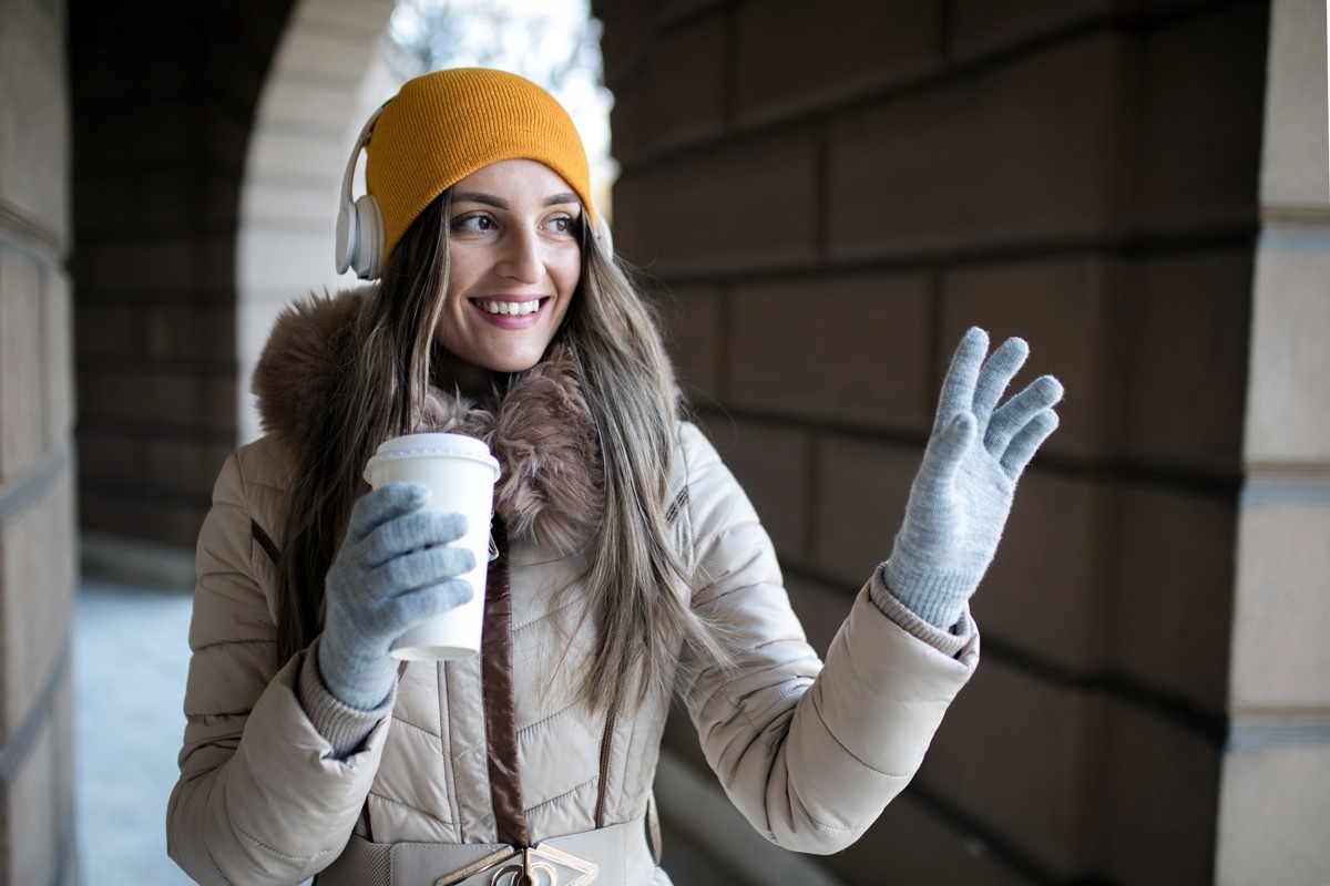 Young woman with coffee to go in winter outside waving