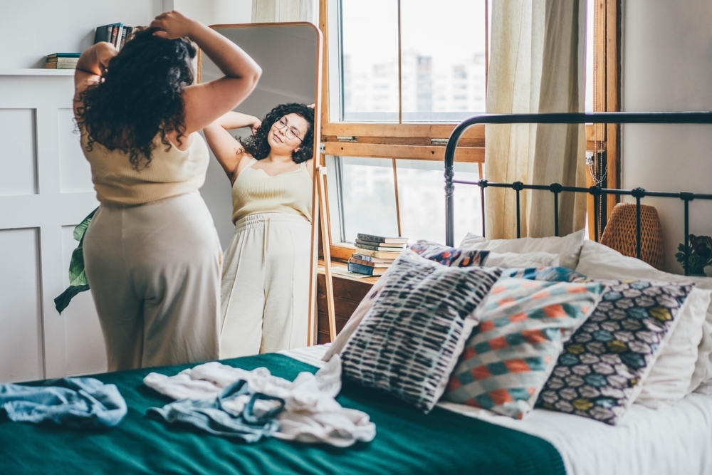 Curly haired curvy woman looking in bedroom mirror