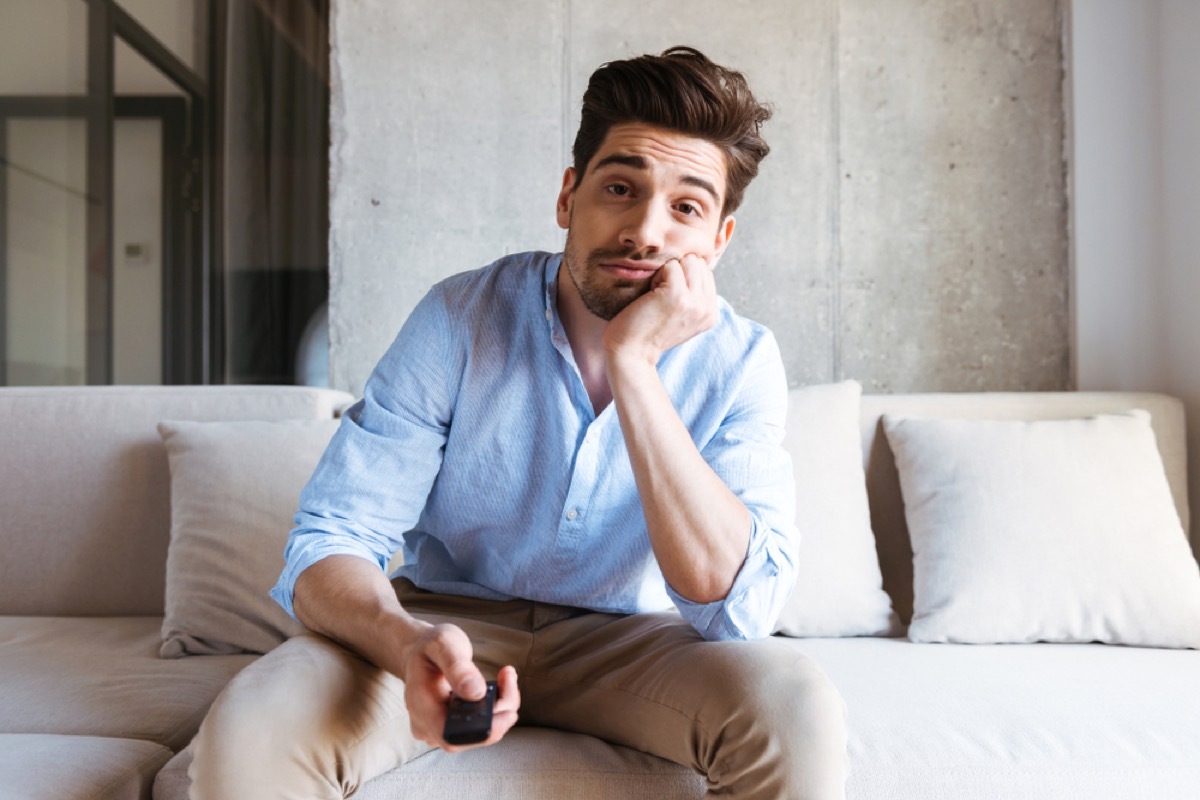 bored white man holding remote and watching tv