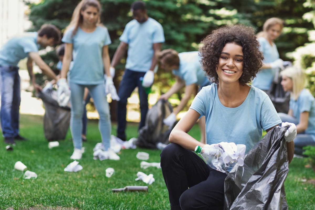 Happy woman and group of volunteers with garbage bags cleaning area in park, copy space