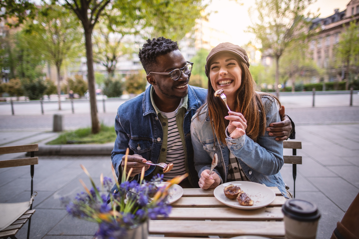 Multiracial couple sitting outside coffee shop and eating some cake