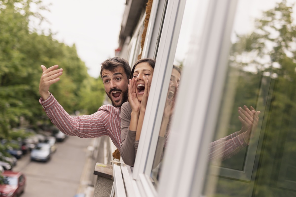 couple waving and shouting out of window in their house