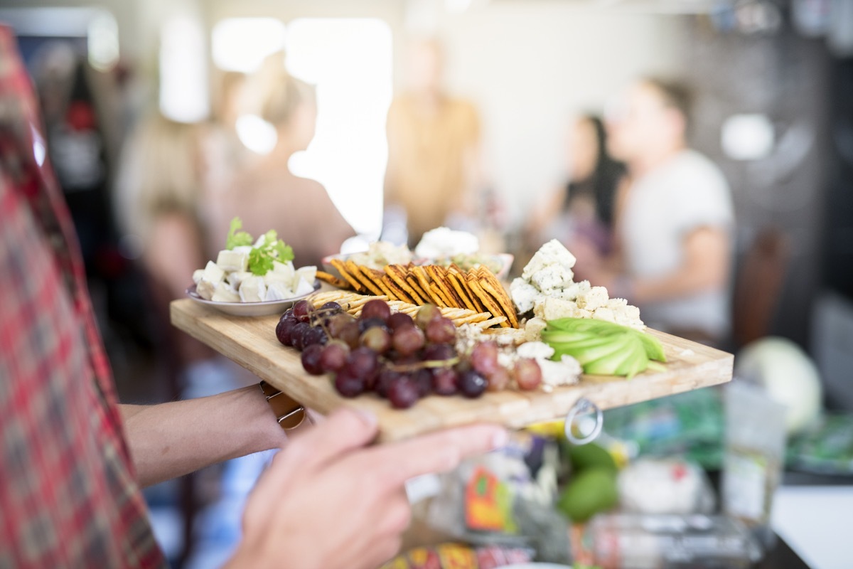 Cropped image of young man holding wooden tray with various vegan food. Male is with healthy meal at social gathering. He is at home.