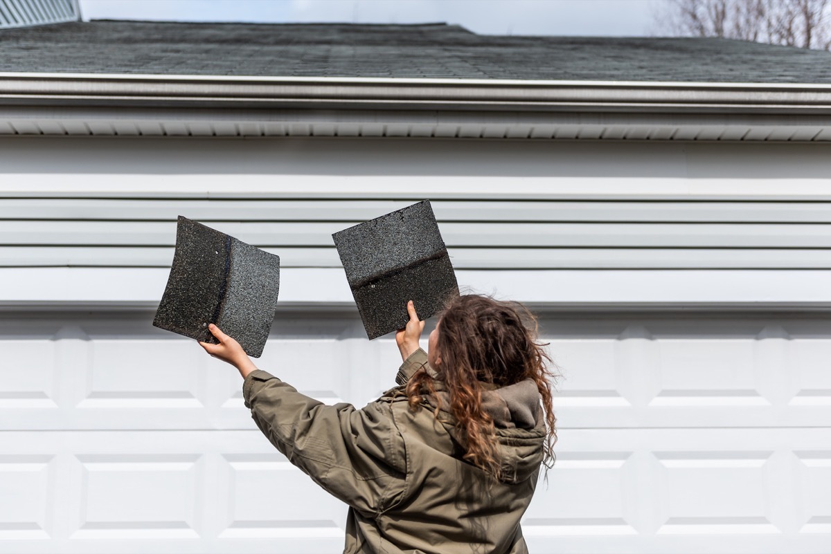 Female homeowner standing in front of house holding two roof tile shingles inspecting damage