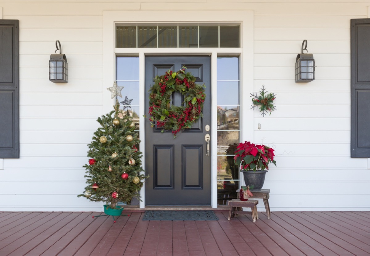 black front door with wreath and mini christmas tree and poinsettia