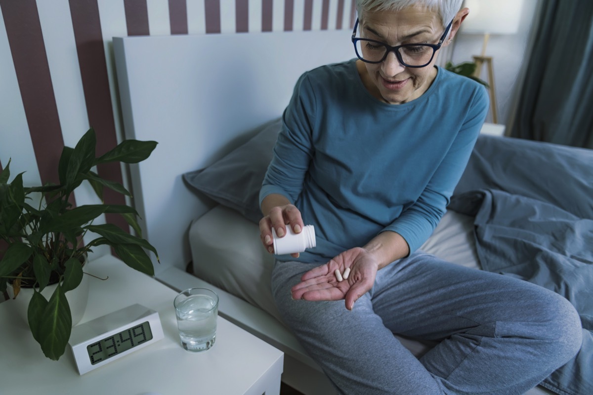 Mature woman taking melatonin supplement pill before bed