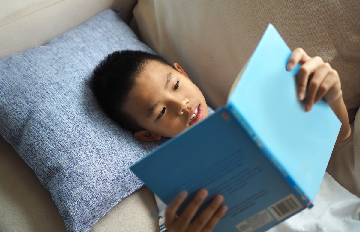 kids reading book while laying on the couch