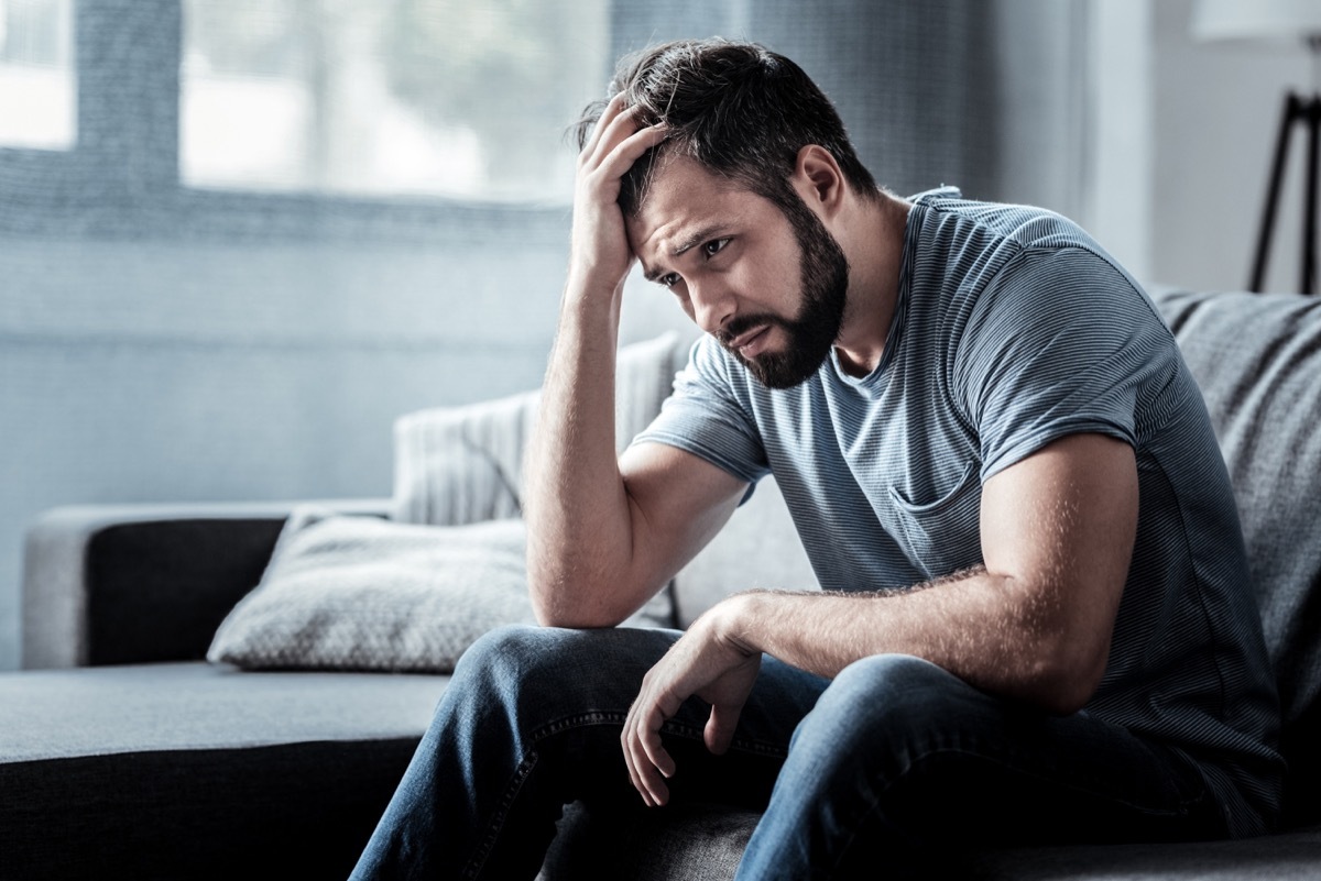 Sad unhappy handsome man sitting on the sofa and holding his forehead while having headache