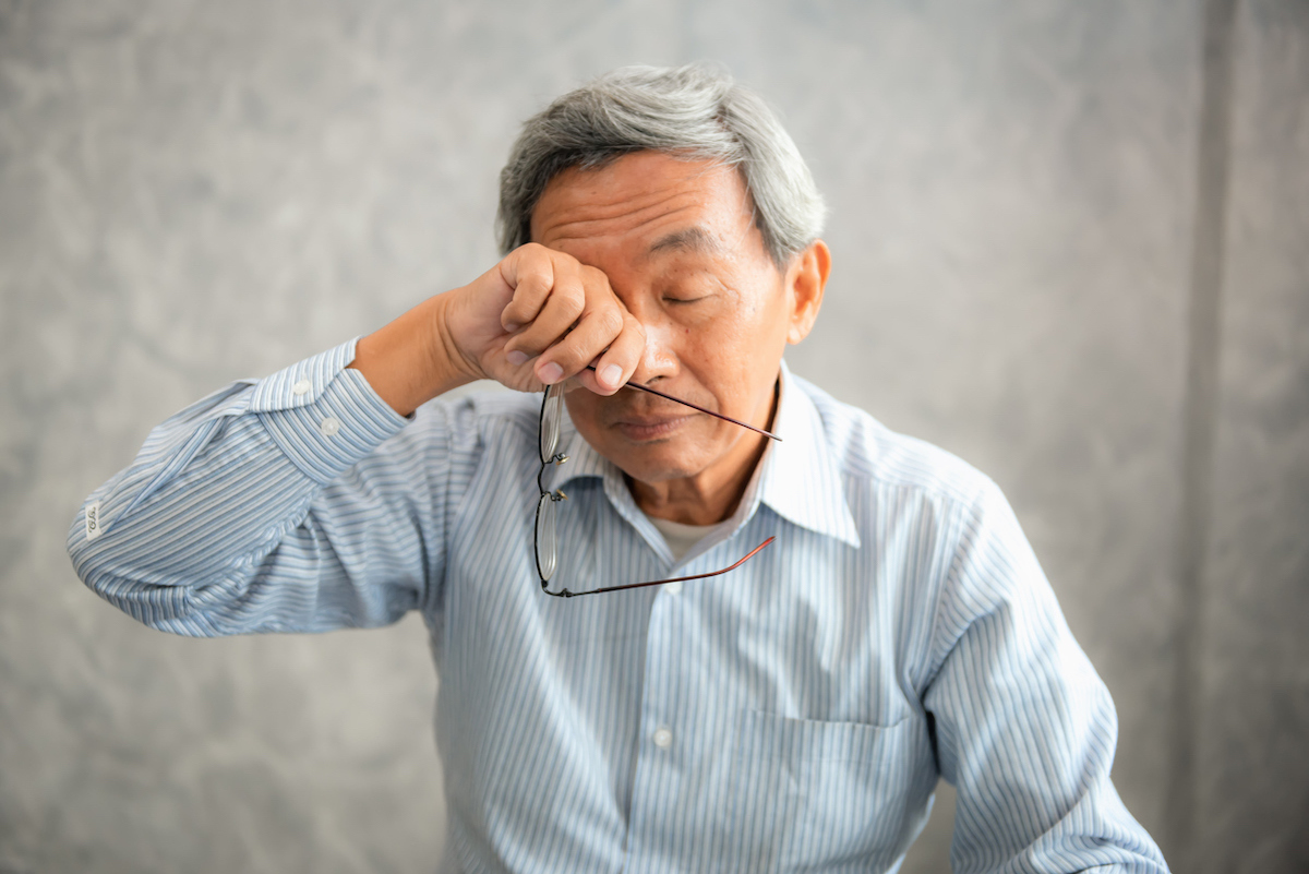 Senior man is holding eyeglasses and rubbing his tired eyes while reading e-book in tablet.