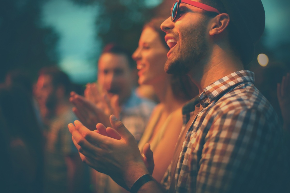 group of people clapping in the dark at what appears to be a concert