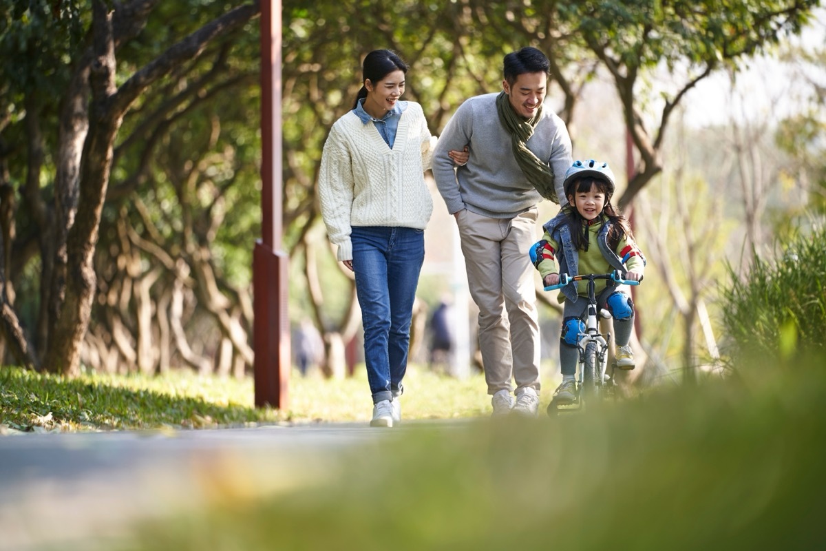 Young family in city park; mother and father are pushing their son on his bike