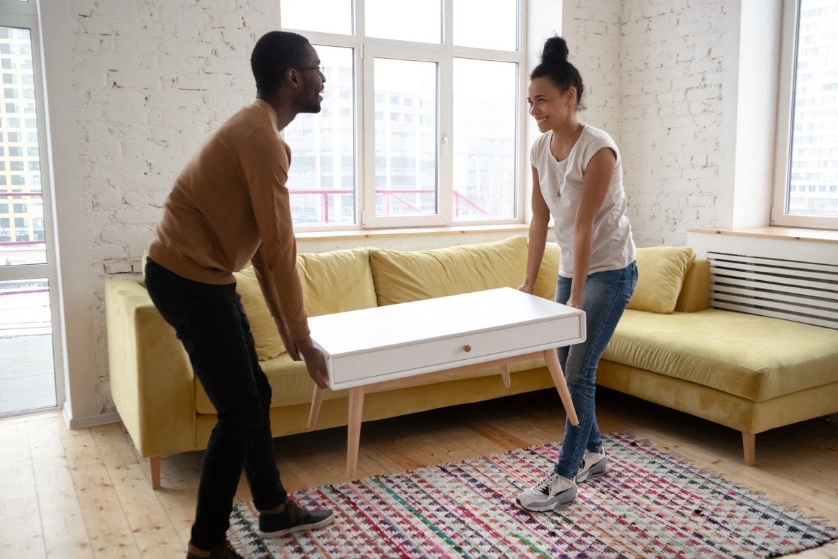 Young happy couple moving wooden table. 