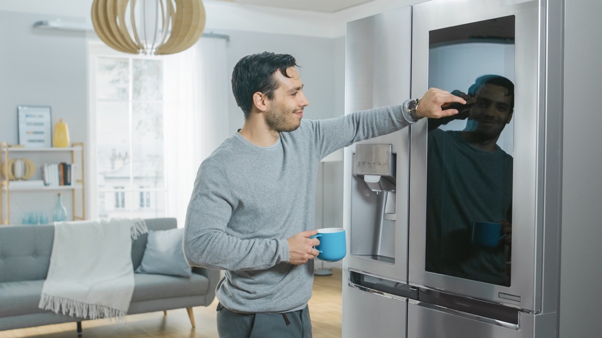 young man touching smart appliance, refrigerator, holding coffee cup