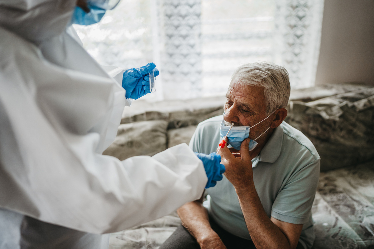 Female doctor in protective suit taking nasal swab test from a senior man