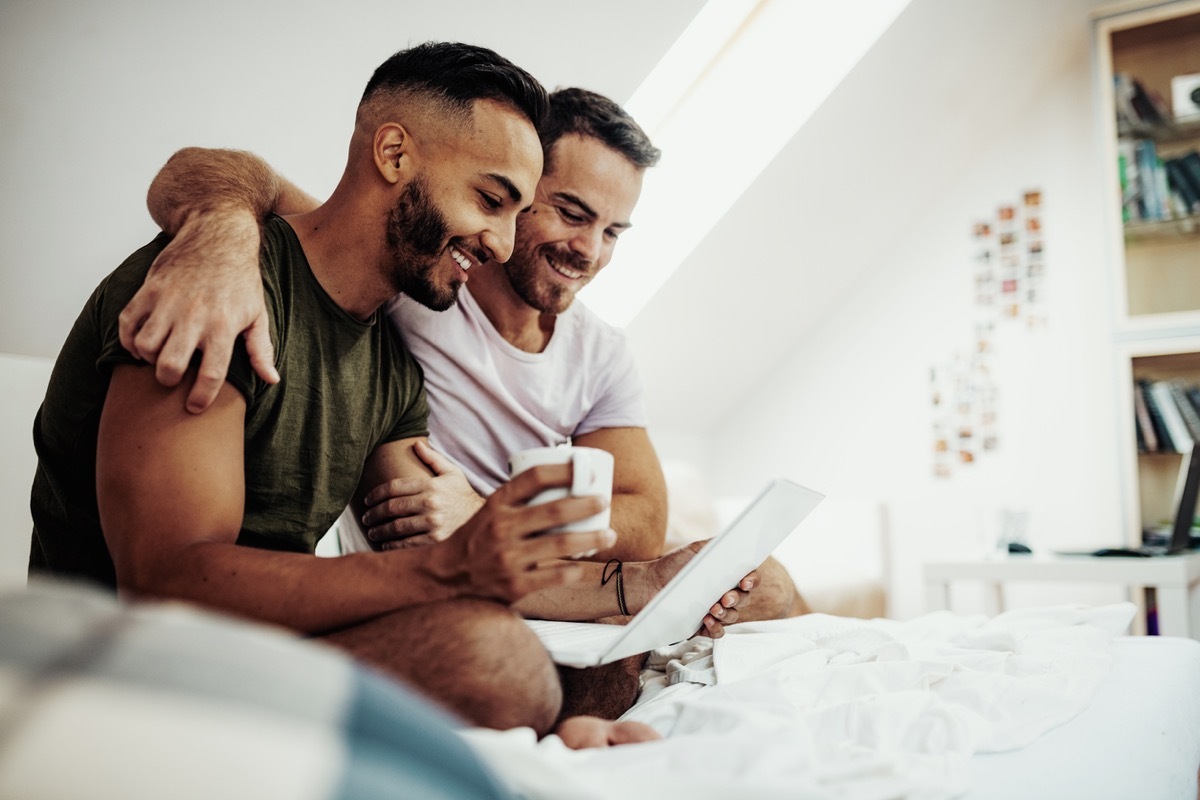 latino man and white man gay couple looking at a computer together on the bed