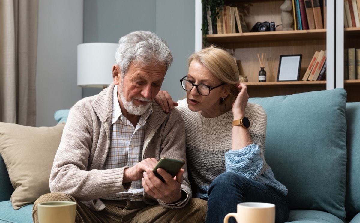 older man and woman reading a good morning text together on the couch